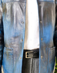 Male model, detail shot, wearing our new Poseidon style, a two-tone black and blue chore jacket, unbuttoned, showing the two-tone colourway and wearing a white dress shirt, a belt and dark pants.