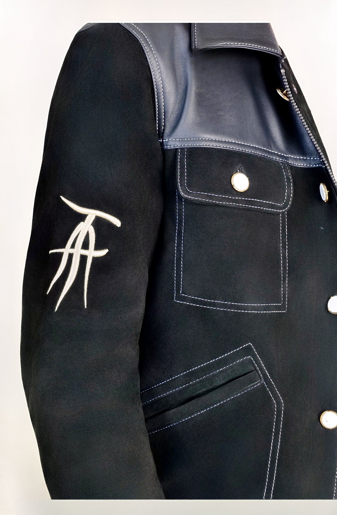 Detail shot, wearing our new Ares style, a Black suede/nubuck trucker jacket with black leather collar, upper front/chest, cuff and base trim showcasing in more detail the mid-sleeve &quot;T&quot; and &quot;A&quot; embroidery detail.