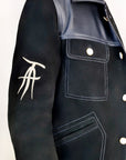 Detail shot, wearing our new Ares style, a Black suede/nubuck trucker jacket with black leather collar, upper front/chest, cuff and base trim showcasing in more detail the mid-sleeve "T" and "A" embroidery detail.