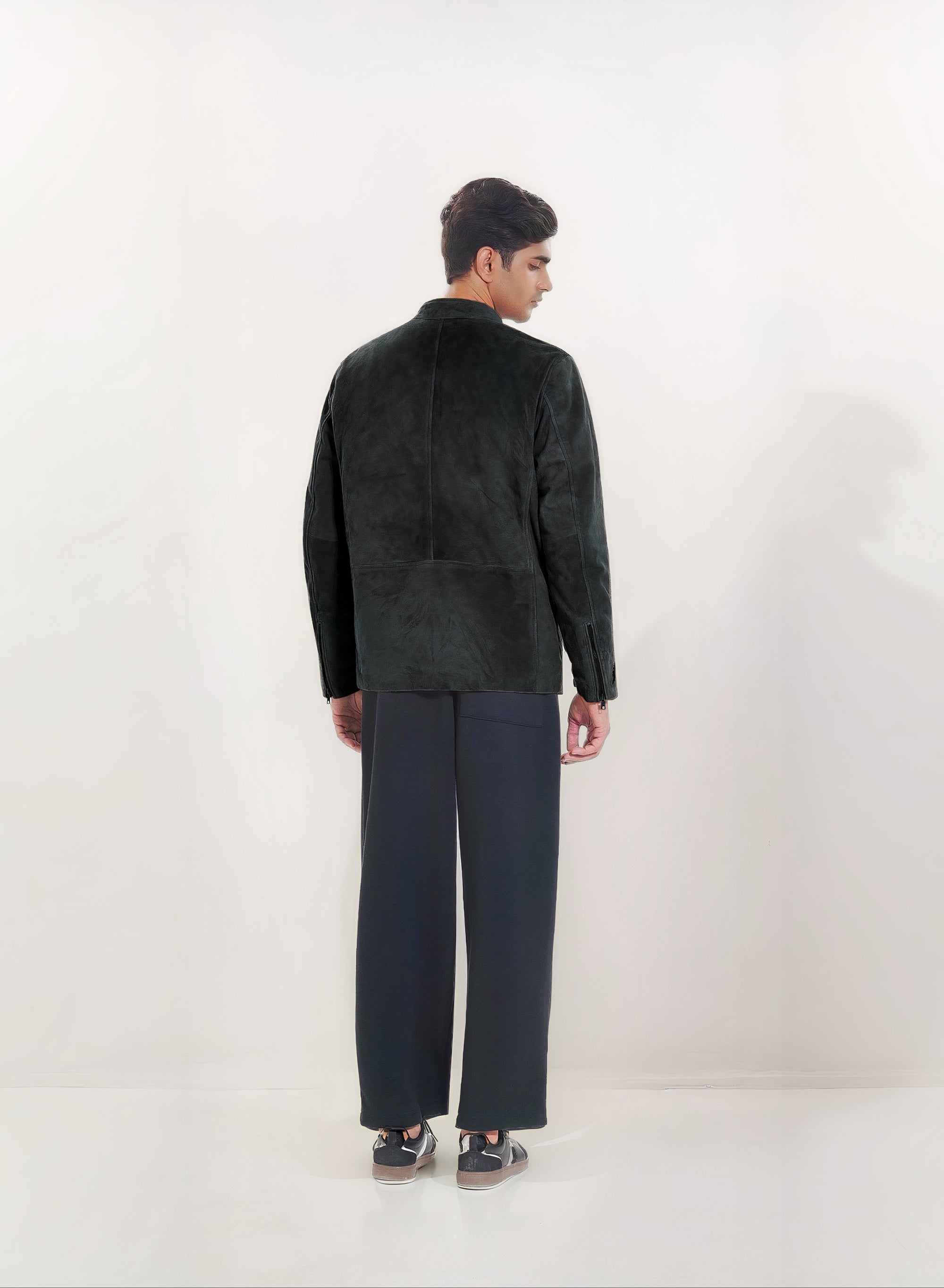 Male model full back shot, wearing our new Achilles style, a Black suede/nubuck racer jacket showcasing embroidery detail, zip cuff closure, and dark pants on a white background.