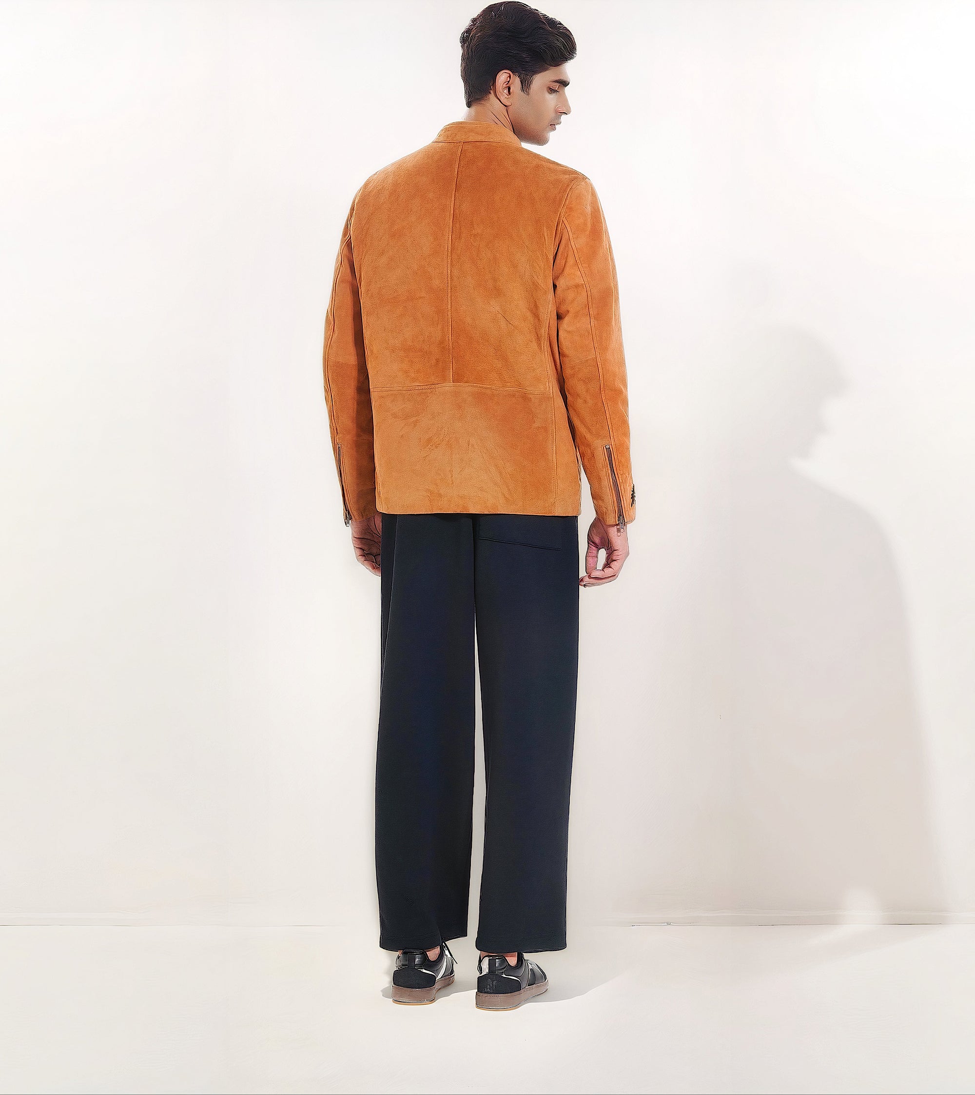 Male model full back shot, wearing our new Achilles style, a Tan suede/nubuck racer jacket showcasing embroidery detail, zip cuff closure, and dark pants on a white background.