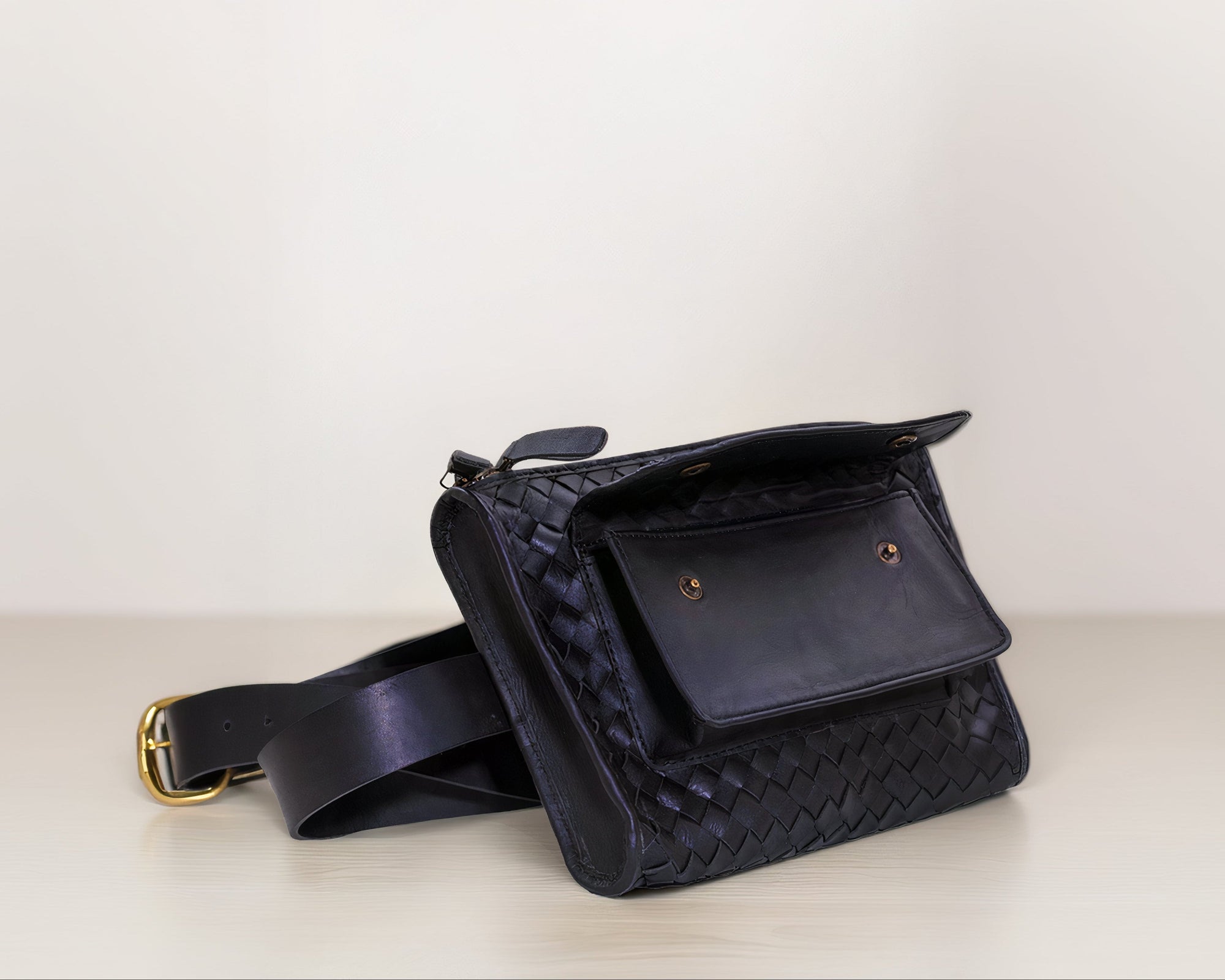 Front shot of our Apollo Loculus black woven belt bag with a front flap open, on a light surface with a white background.