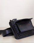 Front shot of our Apollo Loculus black woven belt bag with a front flap open, on a light surface with a white background.