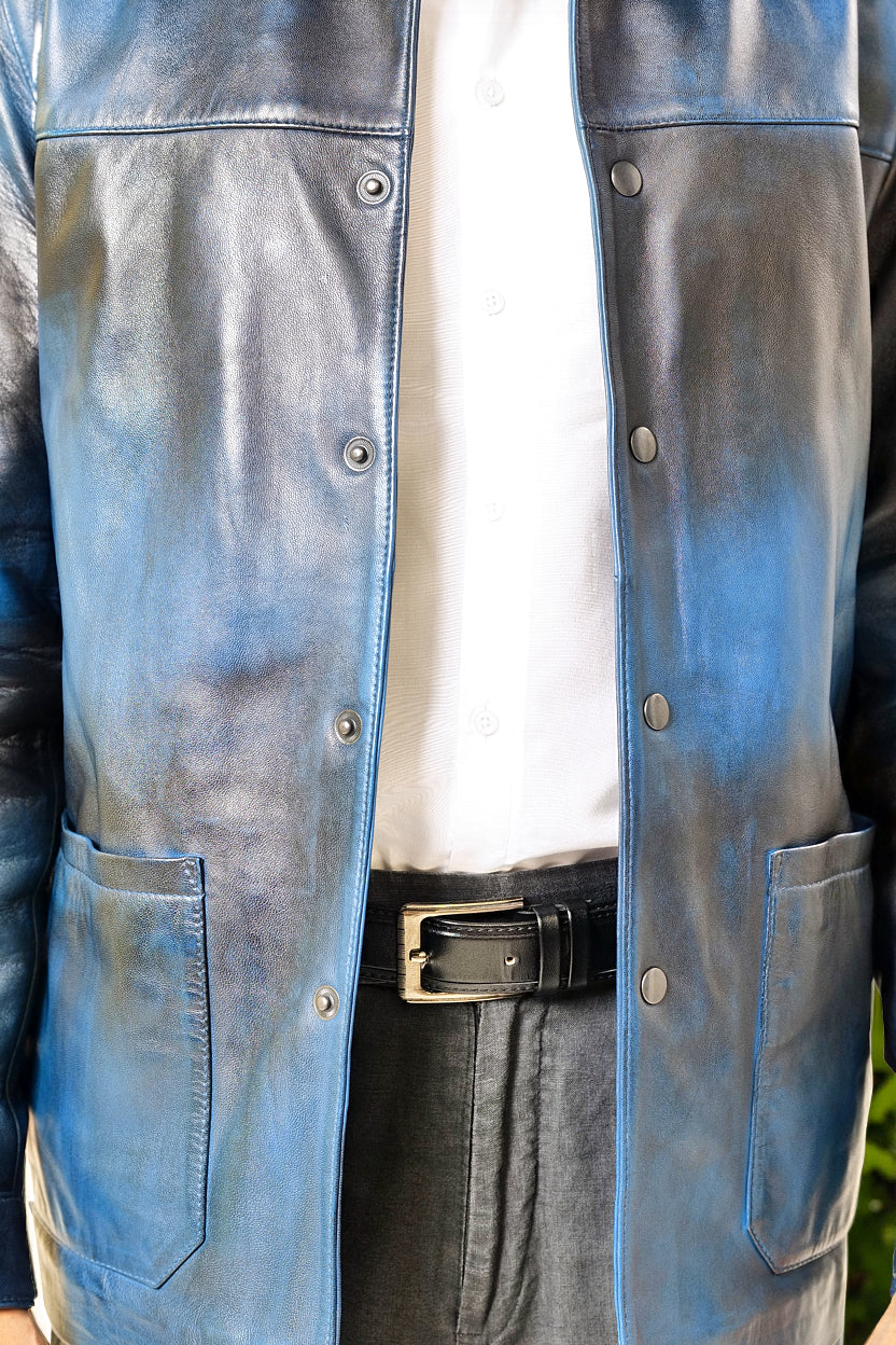 Male model, detail shot, wearing our new Poseidon style, a two-tone black and blue chore jacket, unbuttoned, showing the two-tone colourway and wearing a white dress shirt, a belt and dark pants.