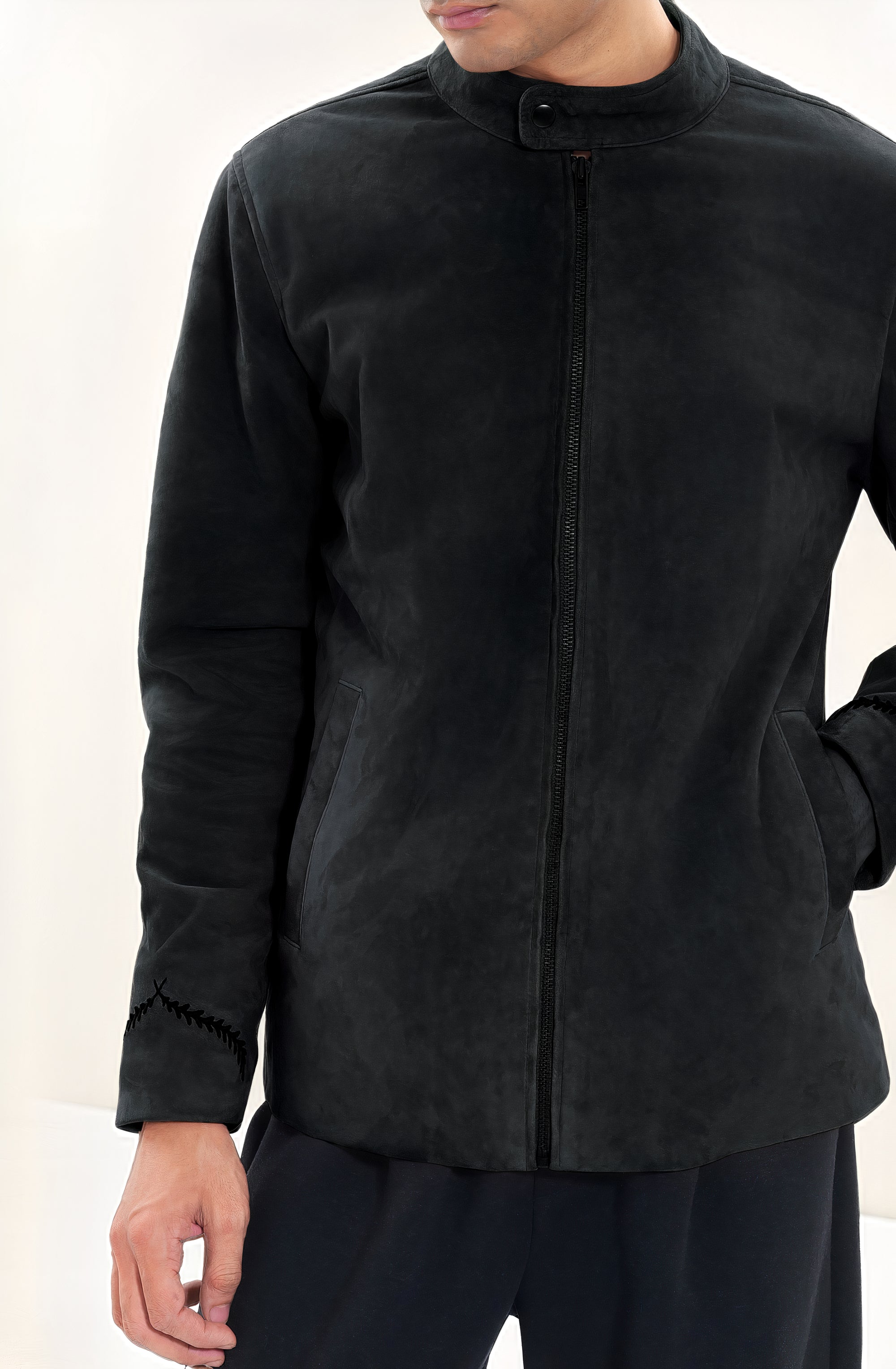 Male model half front shot, wearing our new Achilles style, a Black suede/nubuck racer jacket, zipped all the way up, showcasing embroidery detail, front body zip closure, and dark pants on a white background.