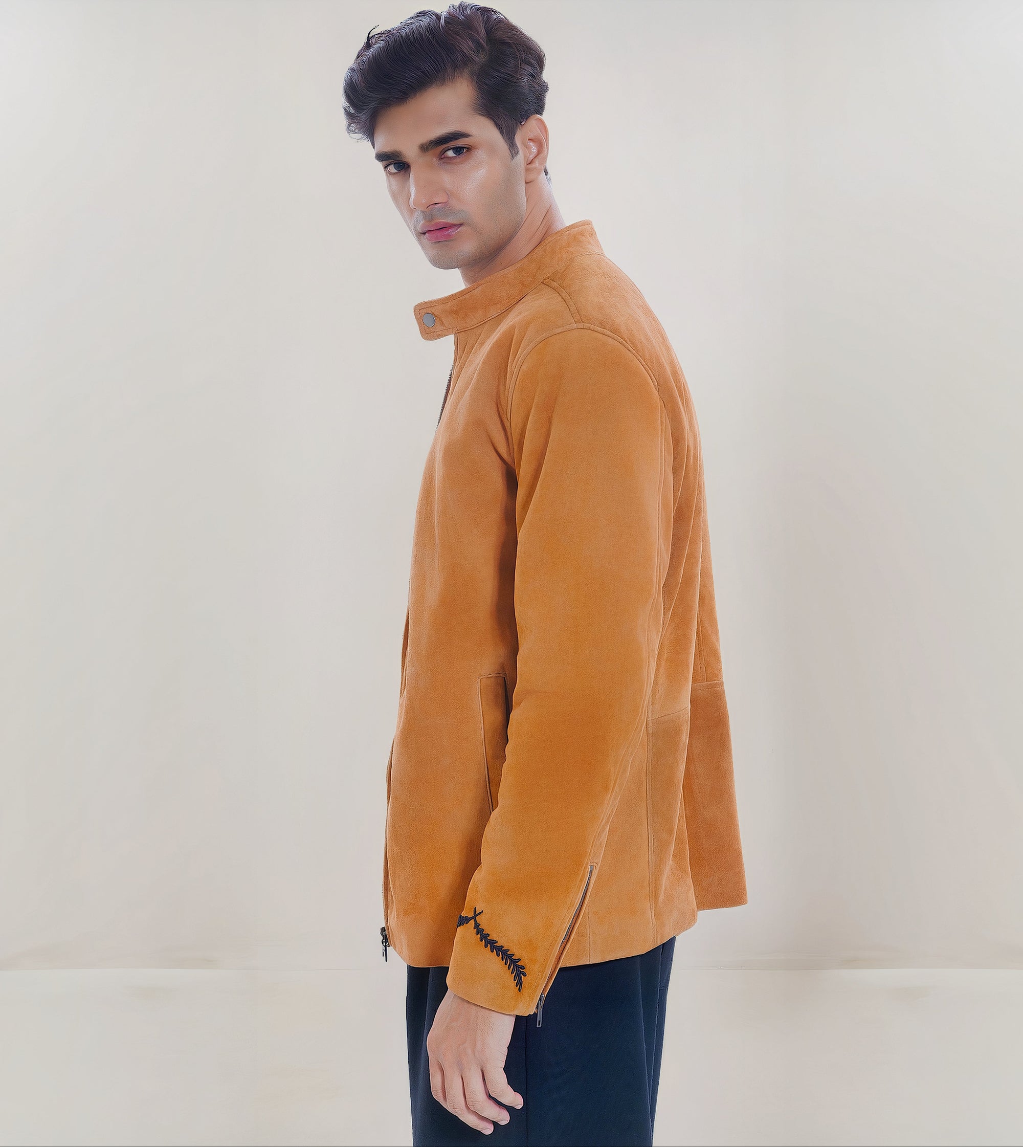 Male model half side shot, wearing our new Achilles style, a Tan suede/nubuck racer jacket showcasing embroidery detail, round snap button collar and dropped shoulder fit.