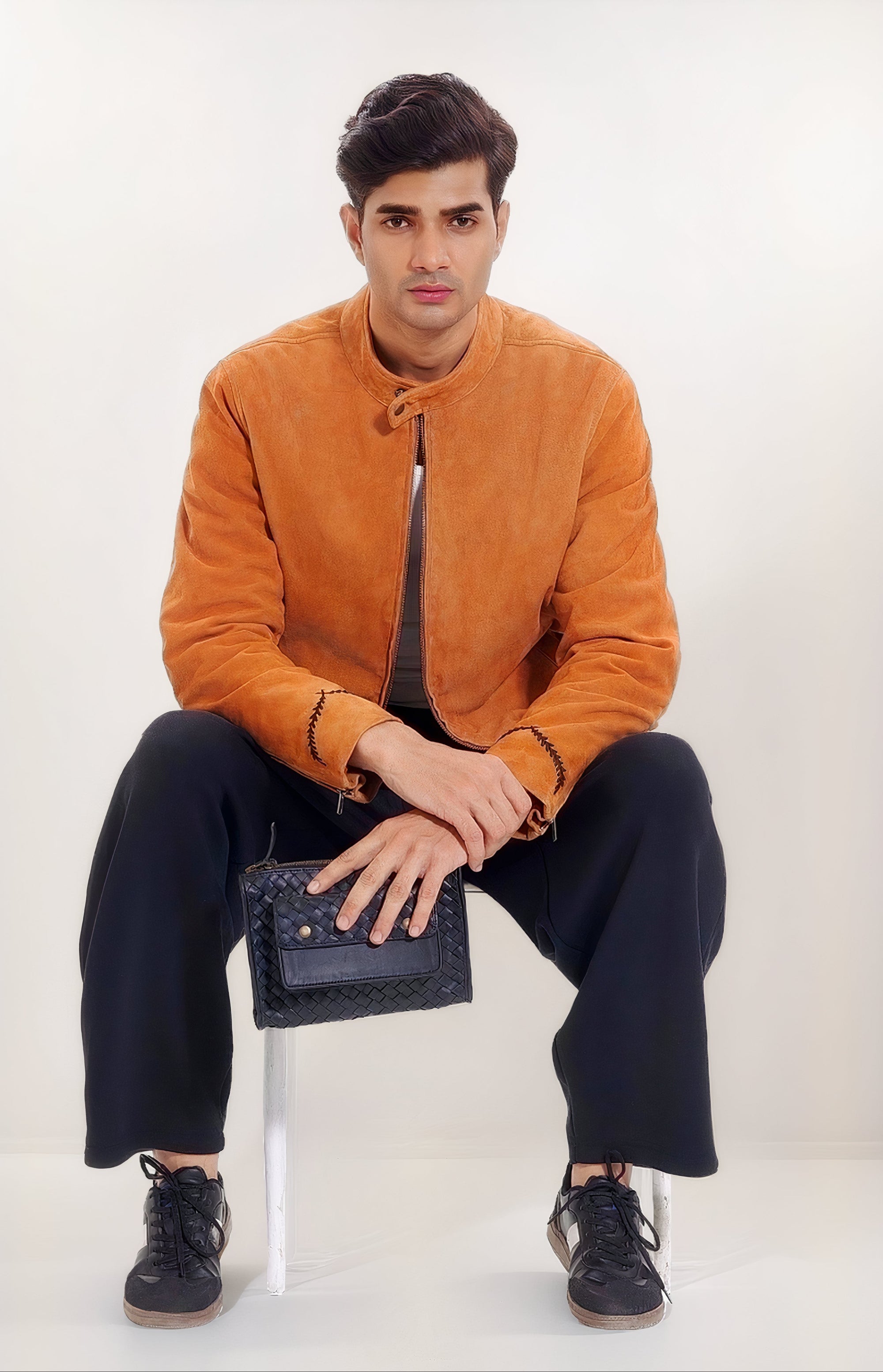 Model shot of our Apollo Loculus black woven belt bag with our male model wearing our Achilles Nubuck Racer jacket in Khaki Tan, holding the belt bag while seated and leaning forward.