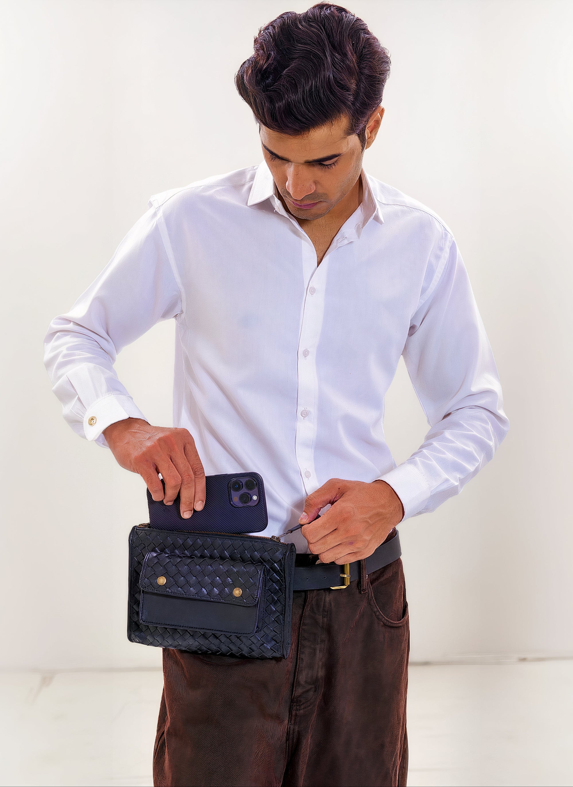 Model shot of our Apollo Loculus black woven belt bag, featuring our male model wearing a white dress shirt and dark dress pants, with the belt bag at his waist where the model is actioning outting his smartphone inside the belt bags interior pocket.
