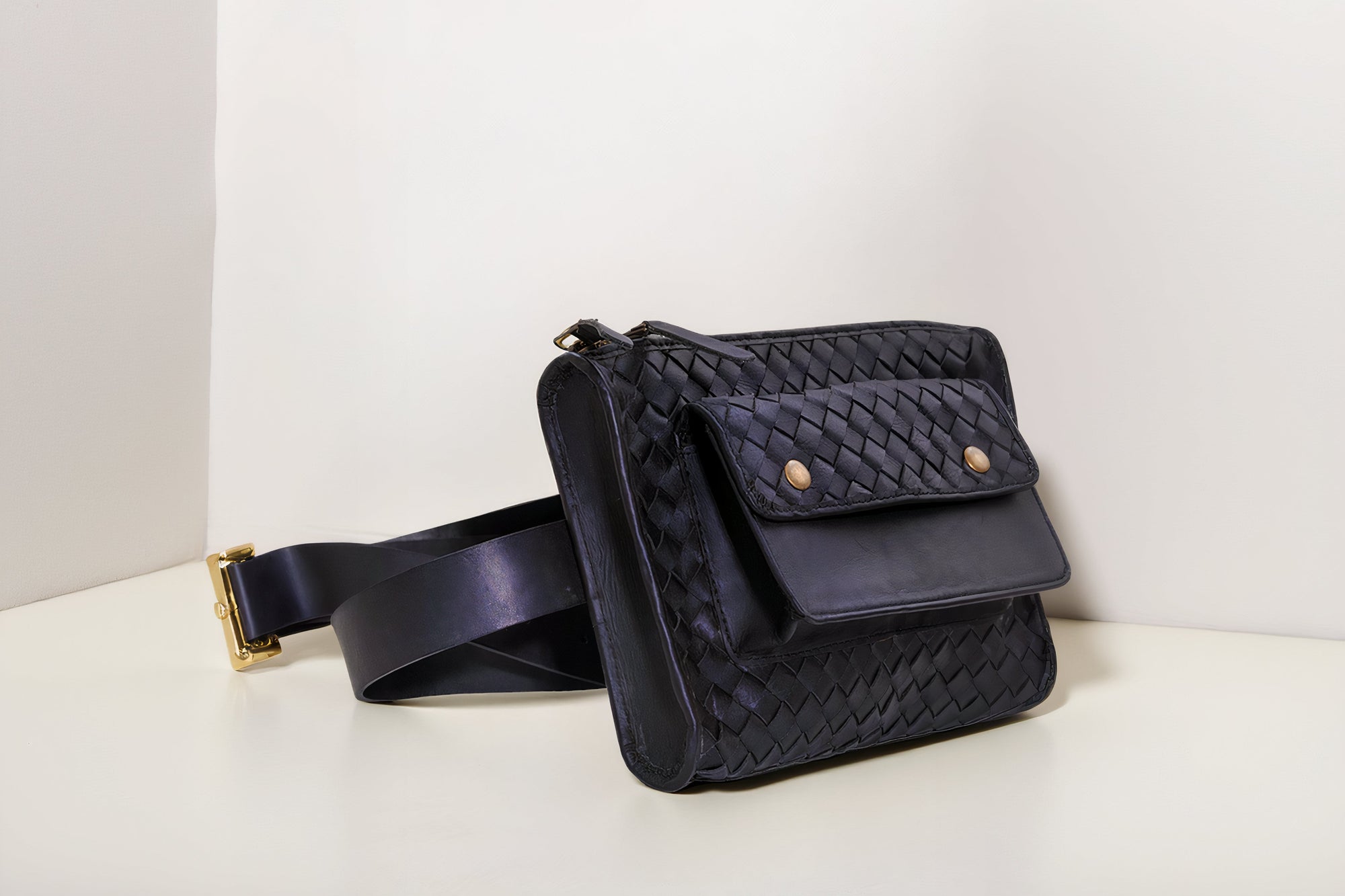Black woven belt bag on a white surface with a light gray background