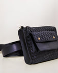 Black woven belt bag on a white surface with a light gray background